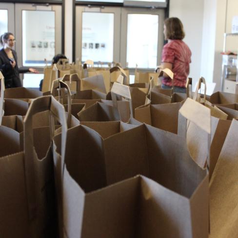 Boynton Health's Nutritious U Food Pantry, paper bags are in the foreground as two students stand in the background assisting with the program